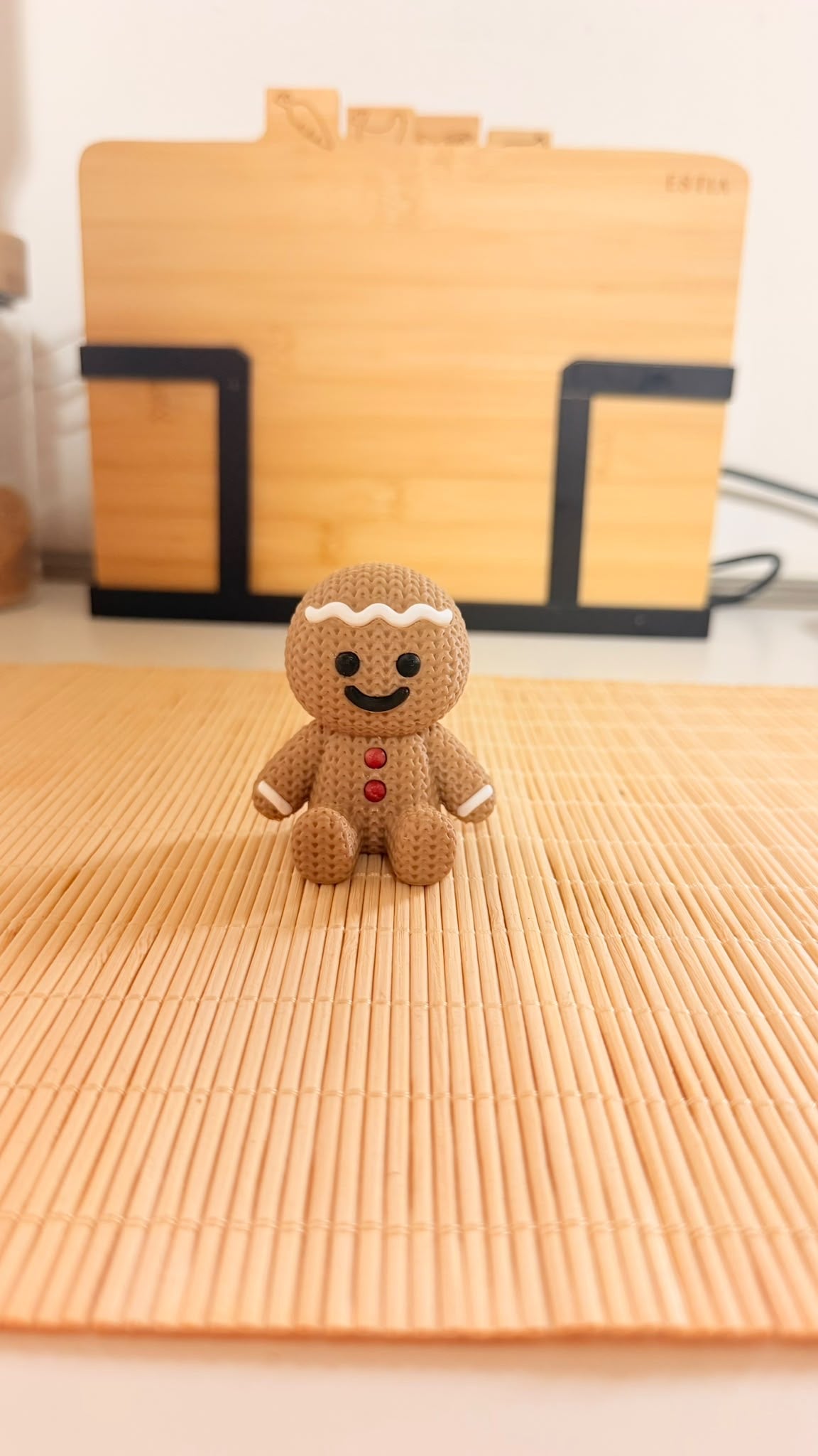 Omino di pan di zenzero natalizio seduto color biscotto, con superficie effetto maglia, dettagli bianchi e due bottoni rossi