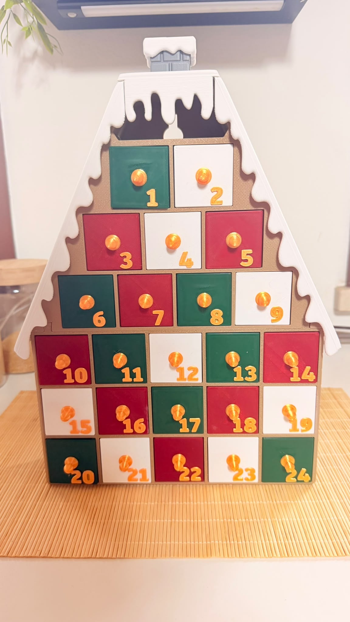 Calendario dell’Avvento artigianale a forma di casetta con tetto innevato e 24 cassetti rossi, verdi e bianchi numerati